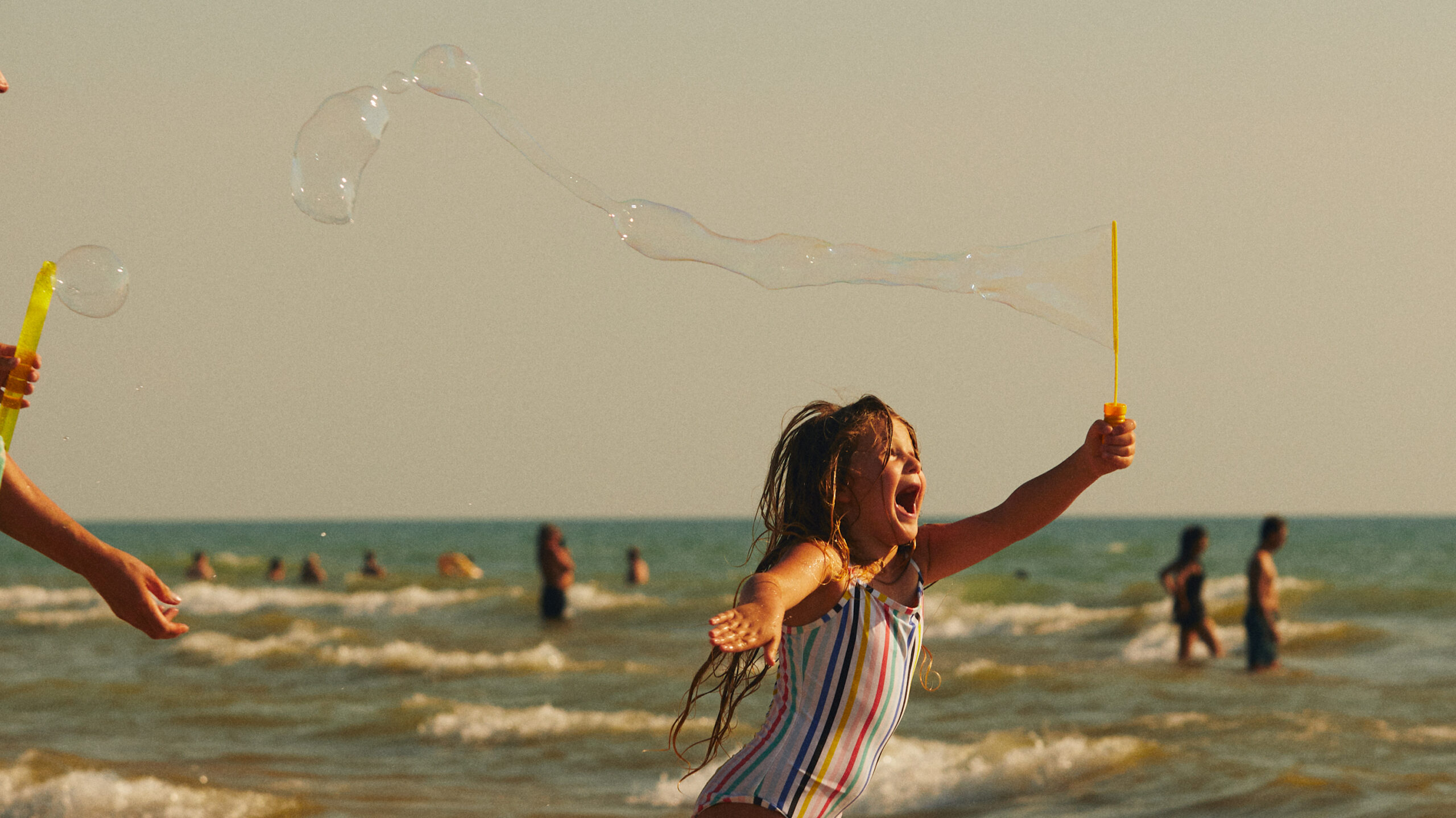A young girl running down the beach blowing bubbles