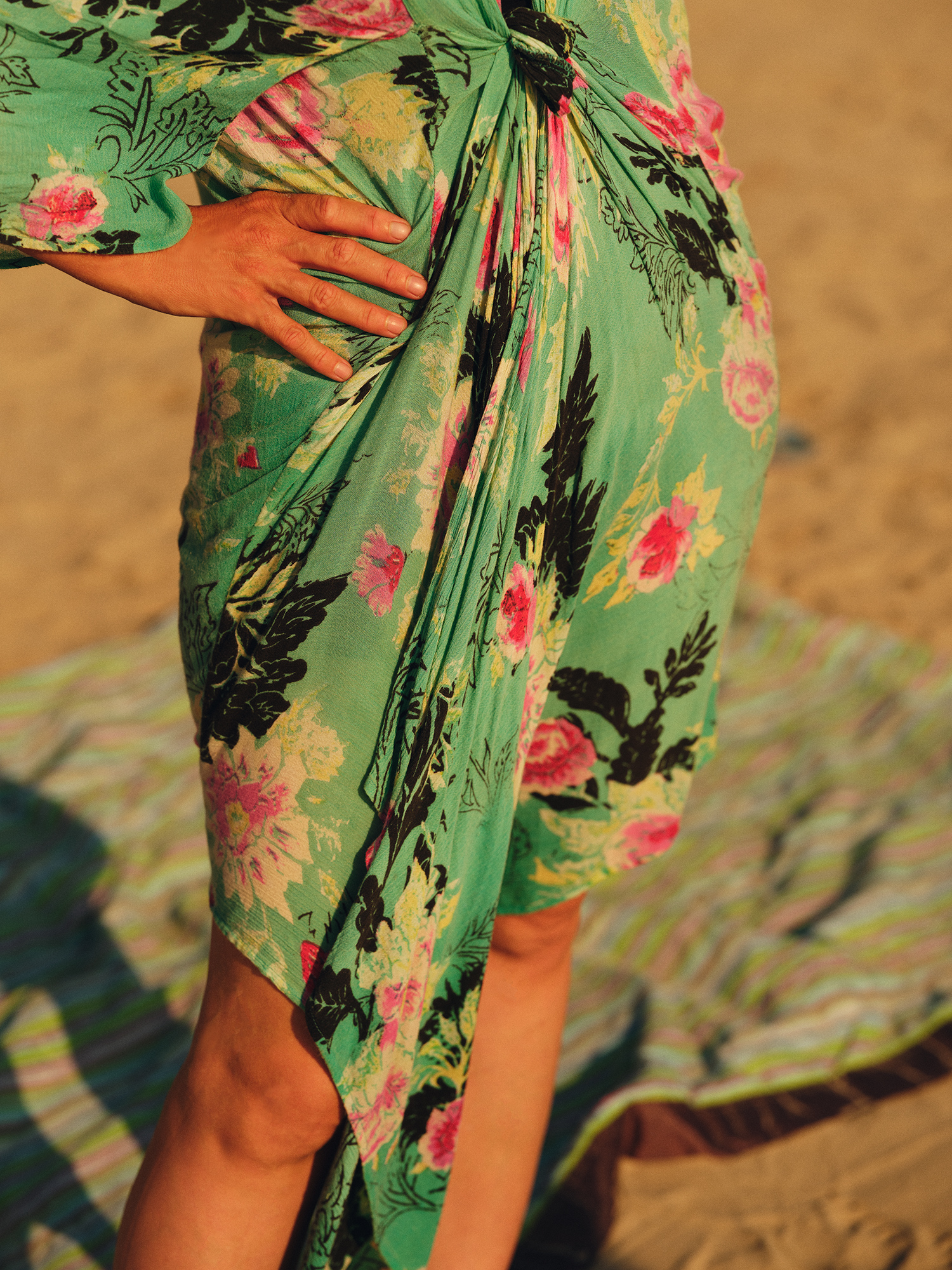 Lower half of a woman standing at the beach in a green dress with flowers on it