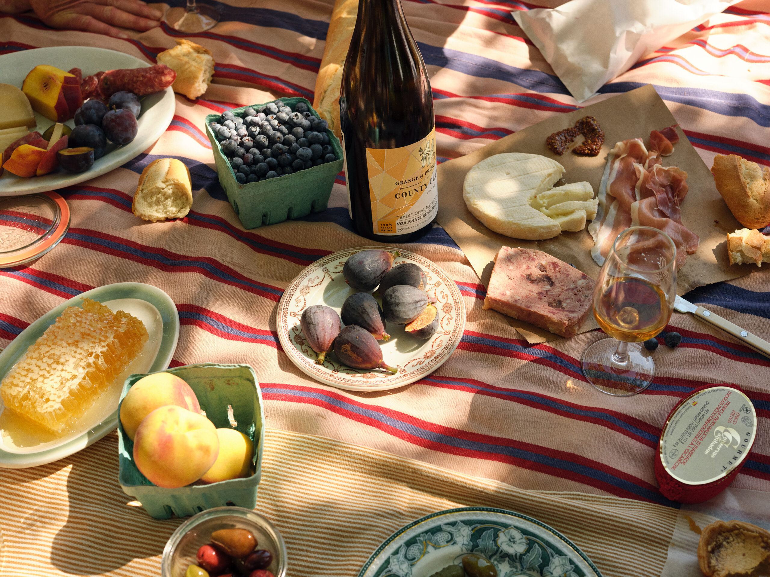 A picnic setup on a striped blanket with a bottle of wine, fruit and cheese