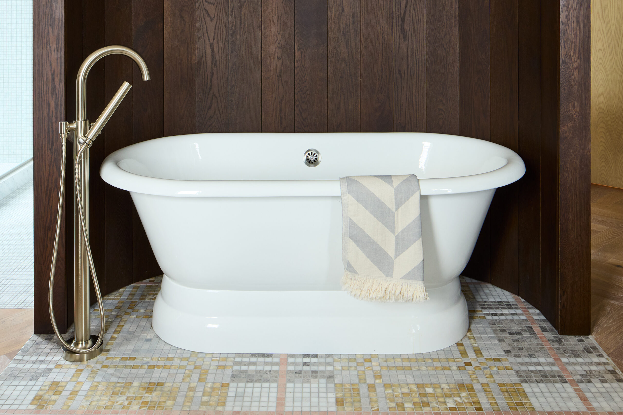 White stand alone tub, on a dark wood panelled background and gold fixtures