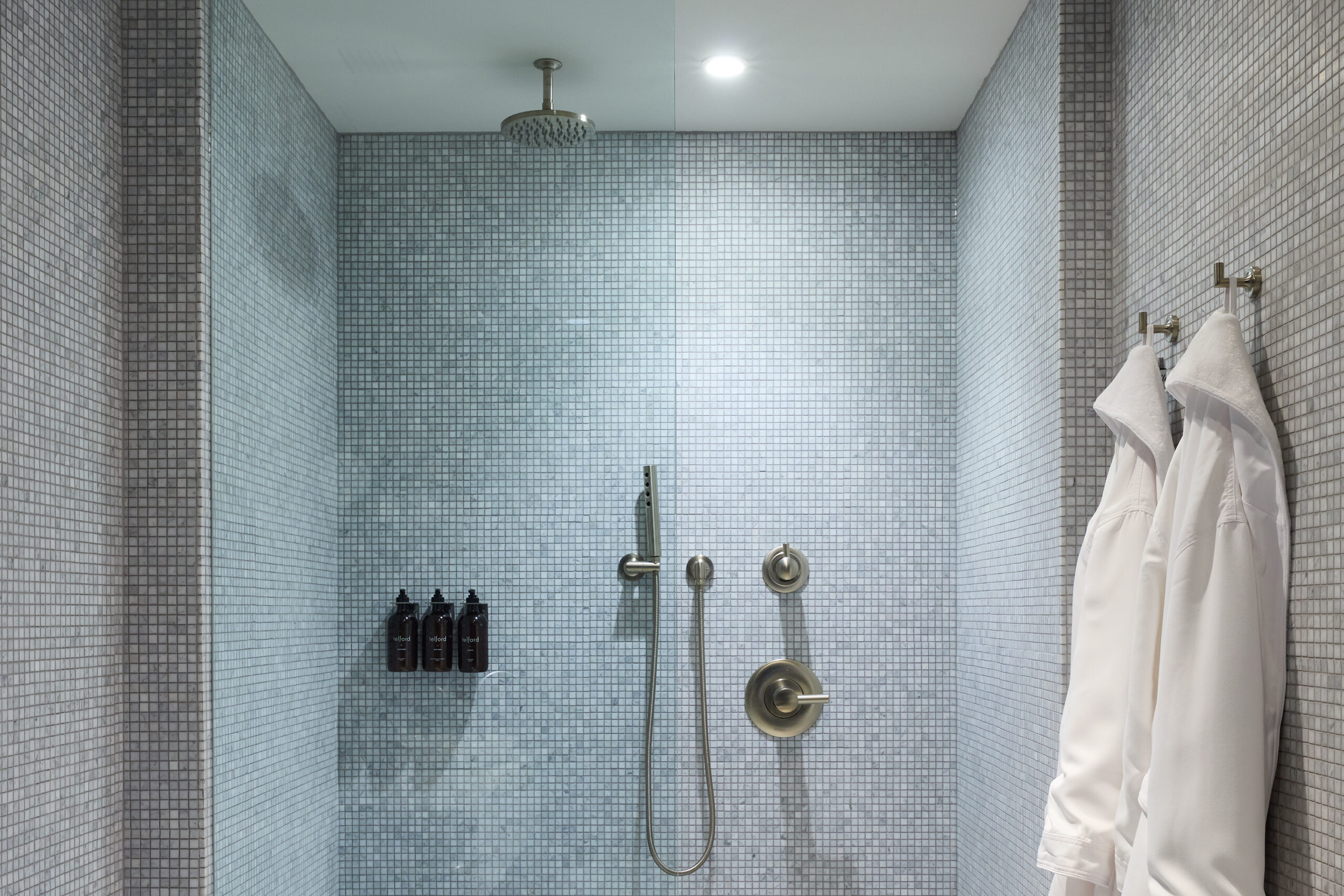 Brightly lit bathroom tiled from floor to ceiling with two white robes