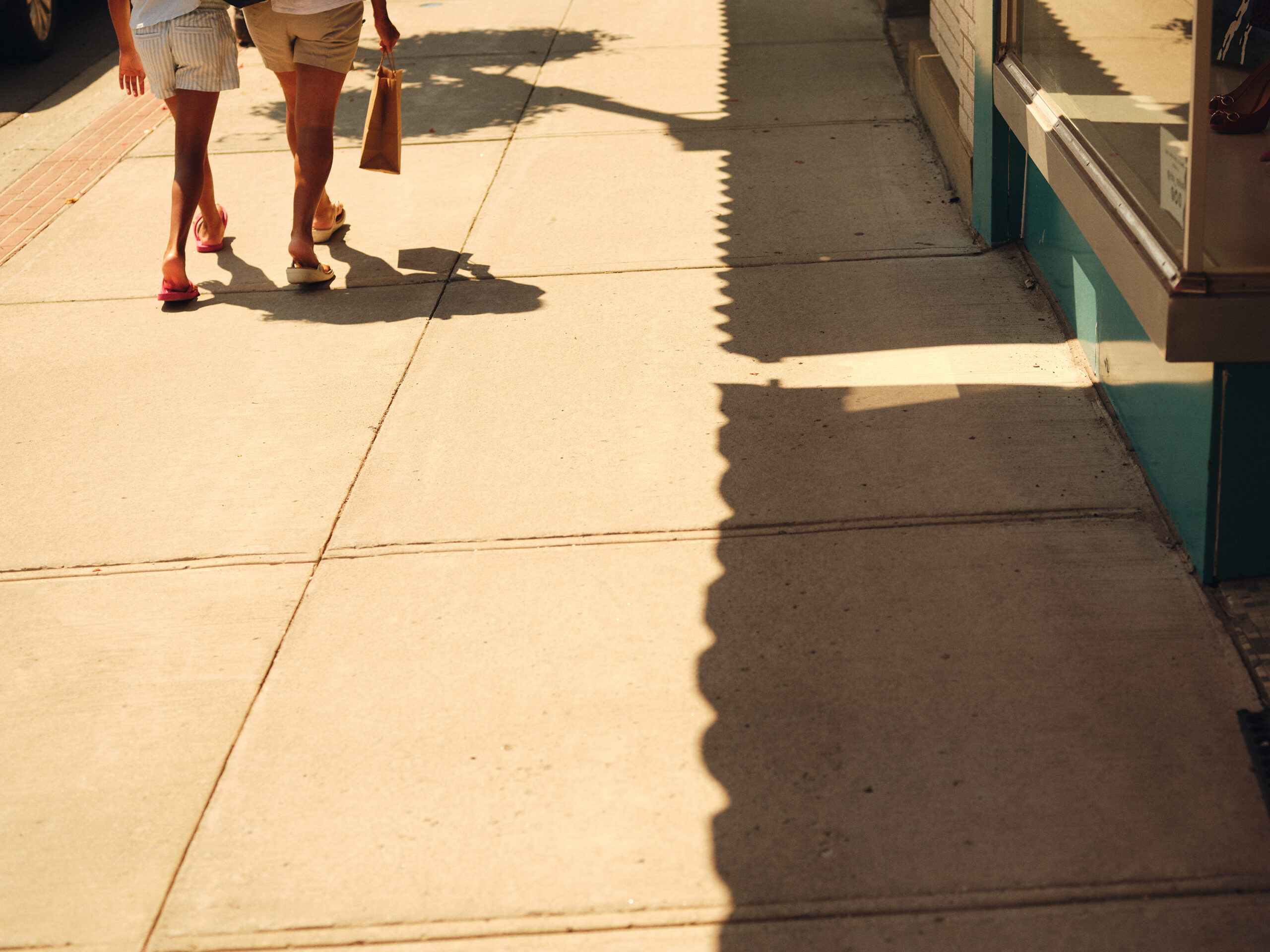 A man and woman walking down a sidewalk with the sun shining