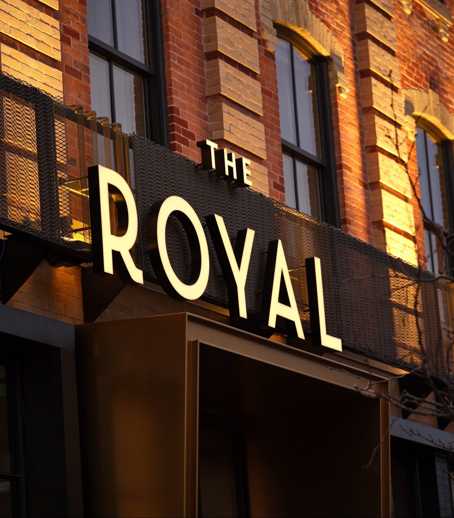 Front of a hotel with The Royal sign soaked in sun, 3 windows above